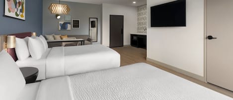A hotel room with two beds, a desk, a television, and artwork on the walls.