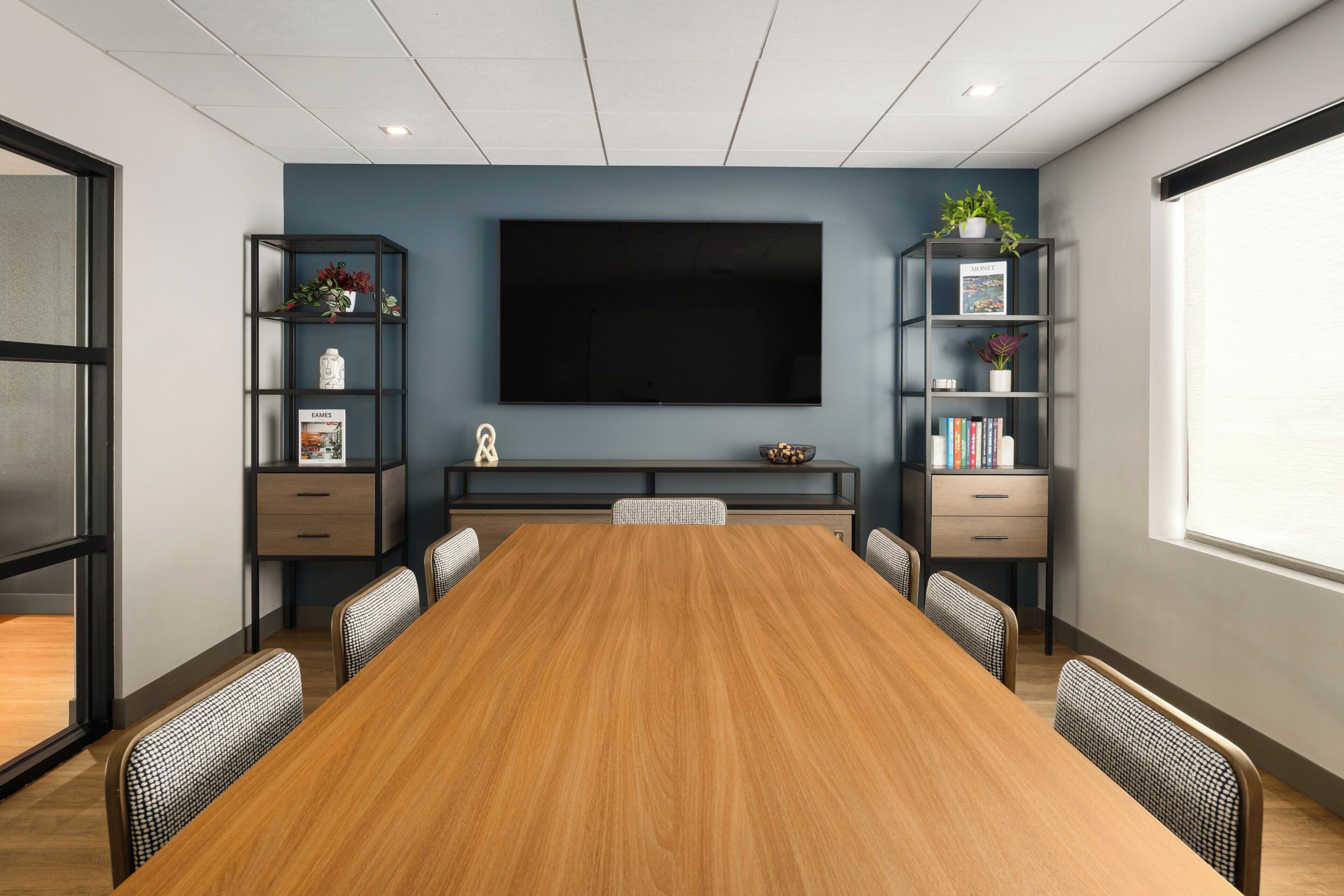 Een vergaderruimte met een grote tafel, stoelen, een flatscreen-tv en boekenkasten met decoratieve objecten.