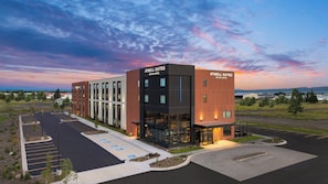 A modern hotel building with a parking lot and a scenic sunset view. - Atwell Suites Belgrade Bozeman Airport by IHG (Belgrade)
