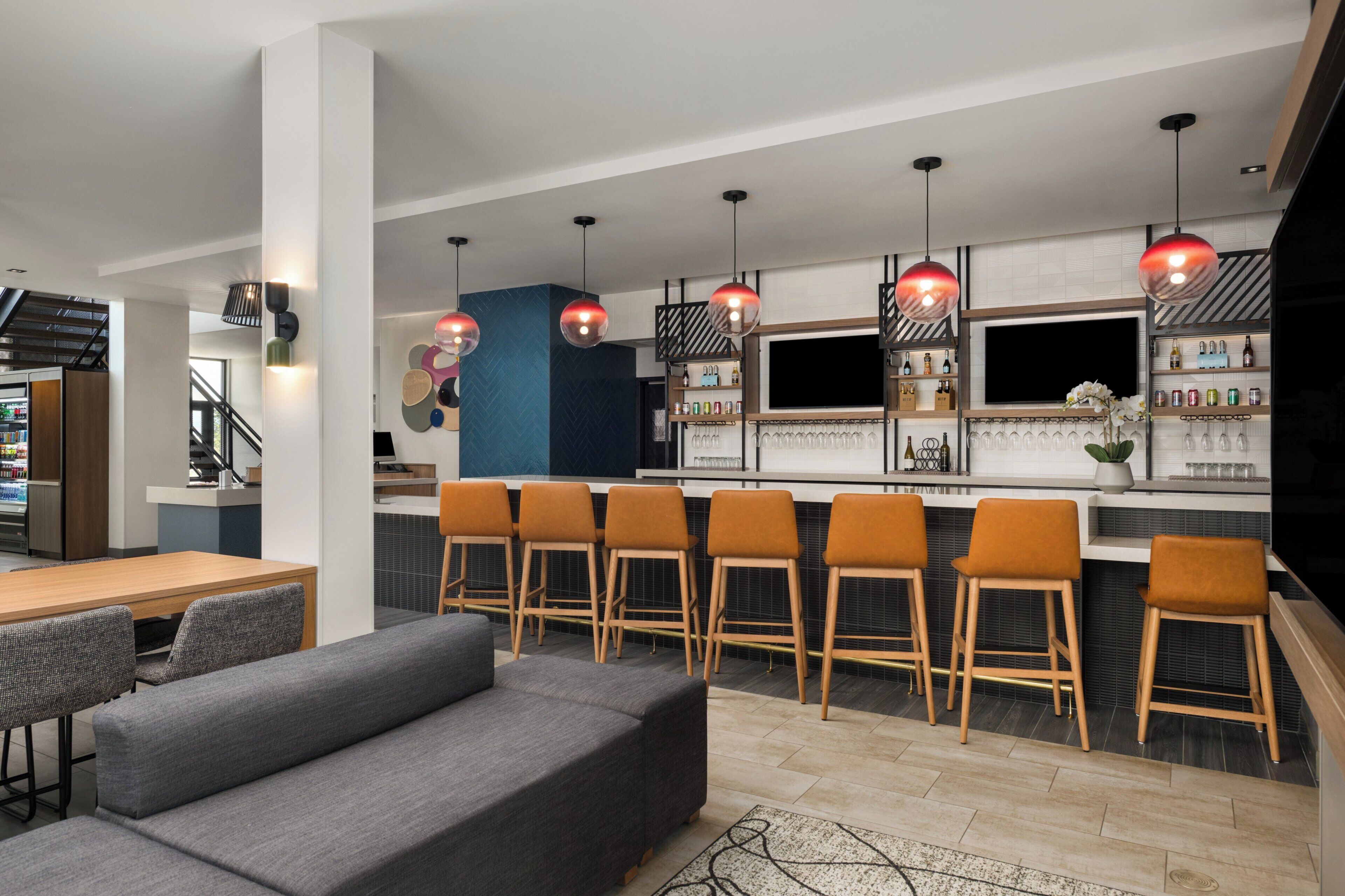A modern kitchen with bar seating, a dining area with a sofa and chairs, and a TV mounted on the wall.