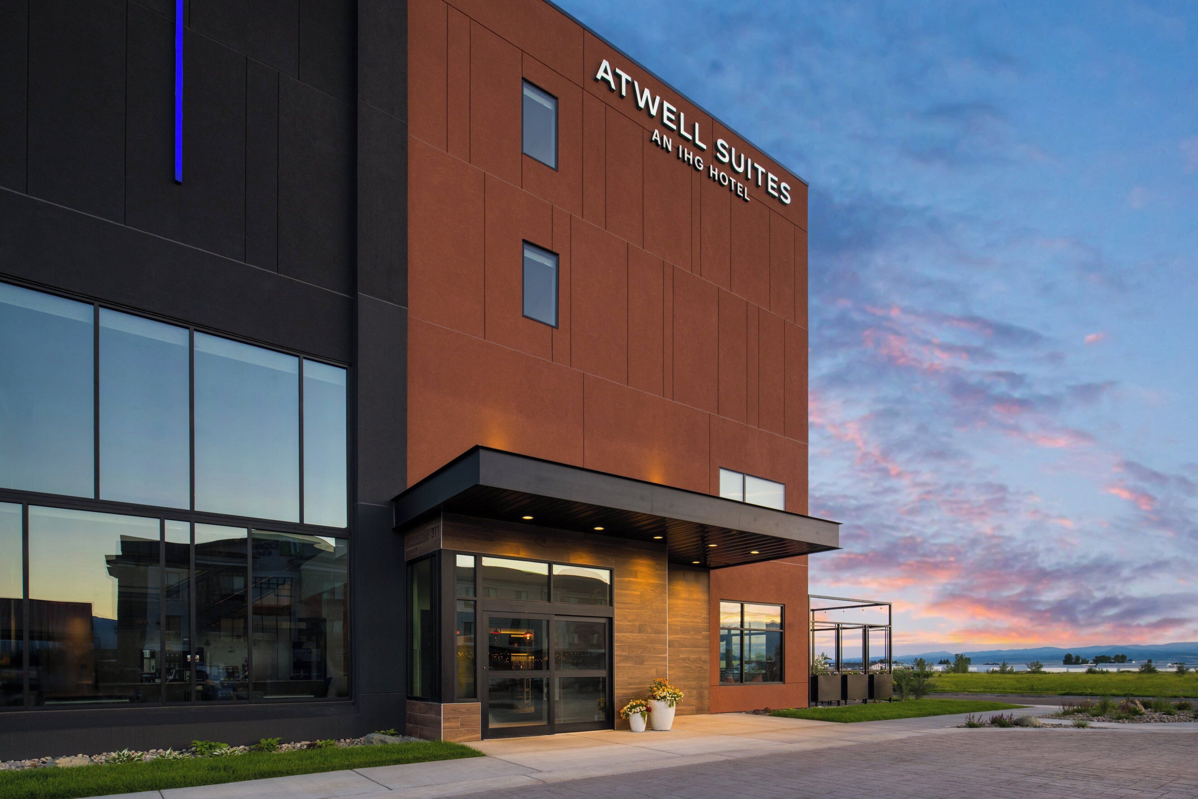 Un hôtel moderne, reconnaissable à son enseigne bien visible indiquant : « ATWELL SUITES, UN HÔTEL IHG ».