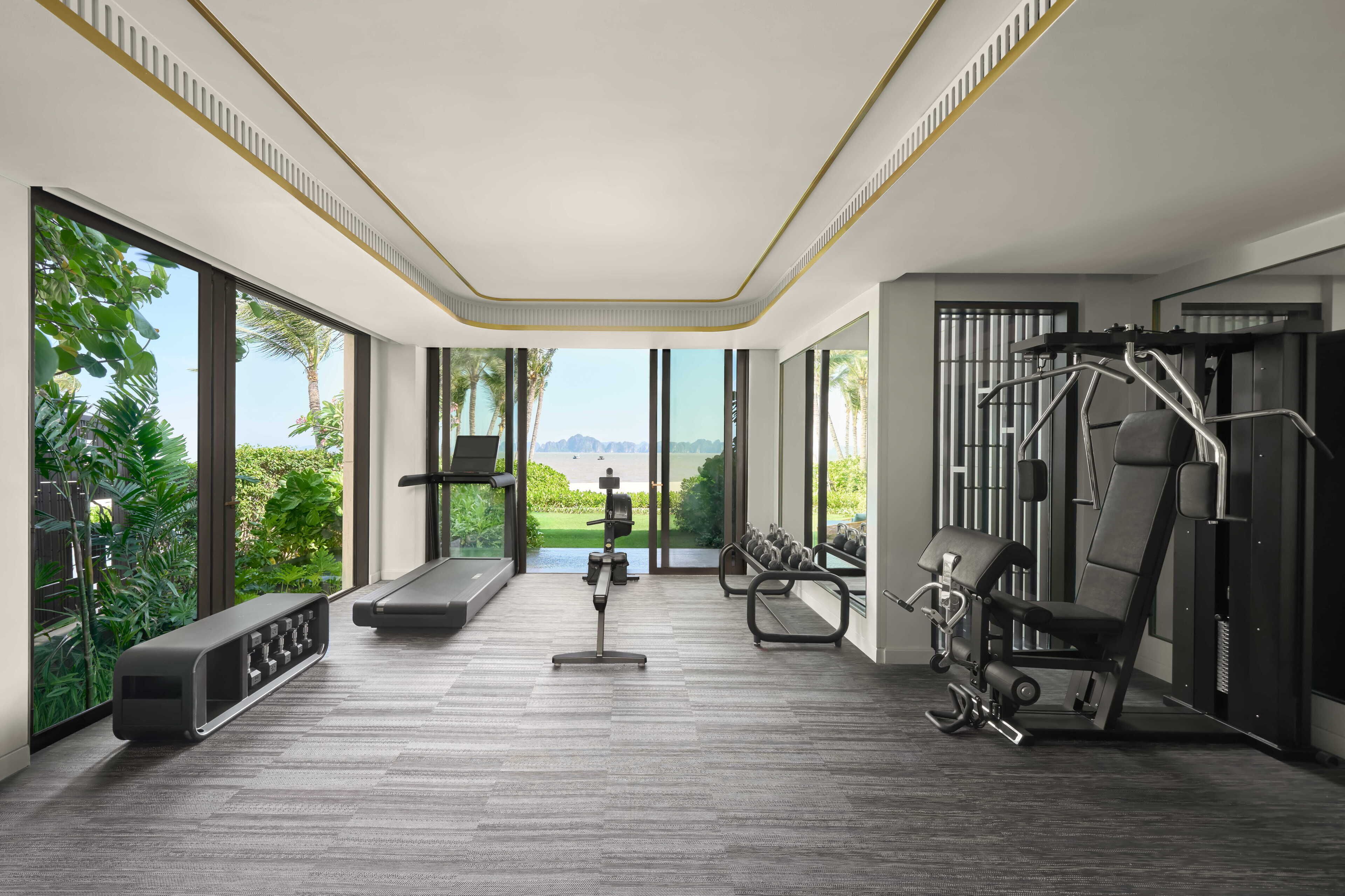 A modern gym with large windows, exercise equipment, and a bench.
