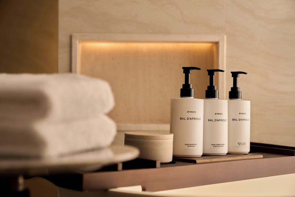 A bathroom vanity with three bottles of BYREDO BAL D'AFRIQUE hair products and a folded towel.