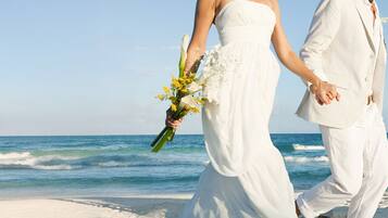 Una pareja camina de la mano por una playa sosteniendo un ramo de flores.