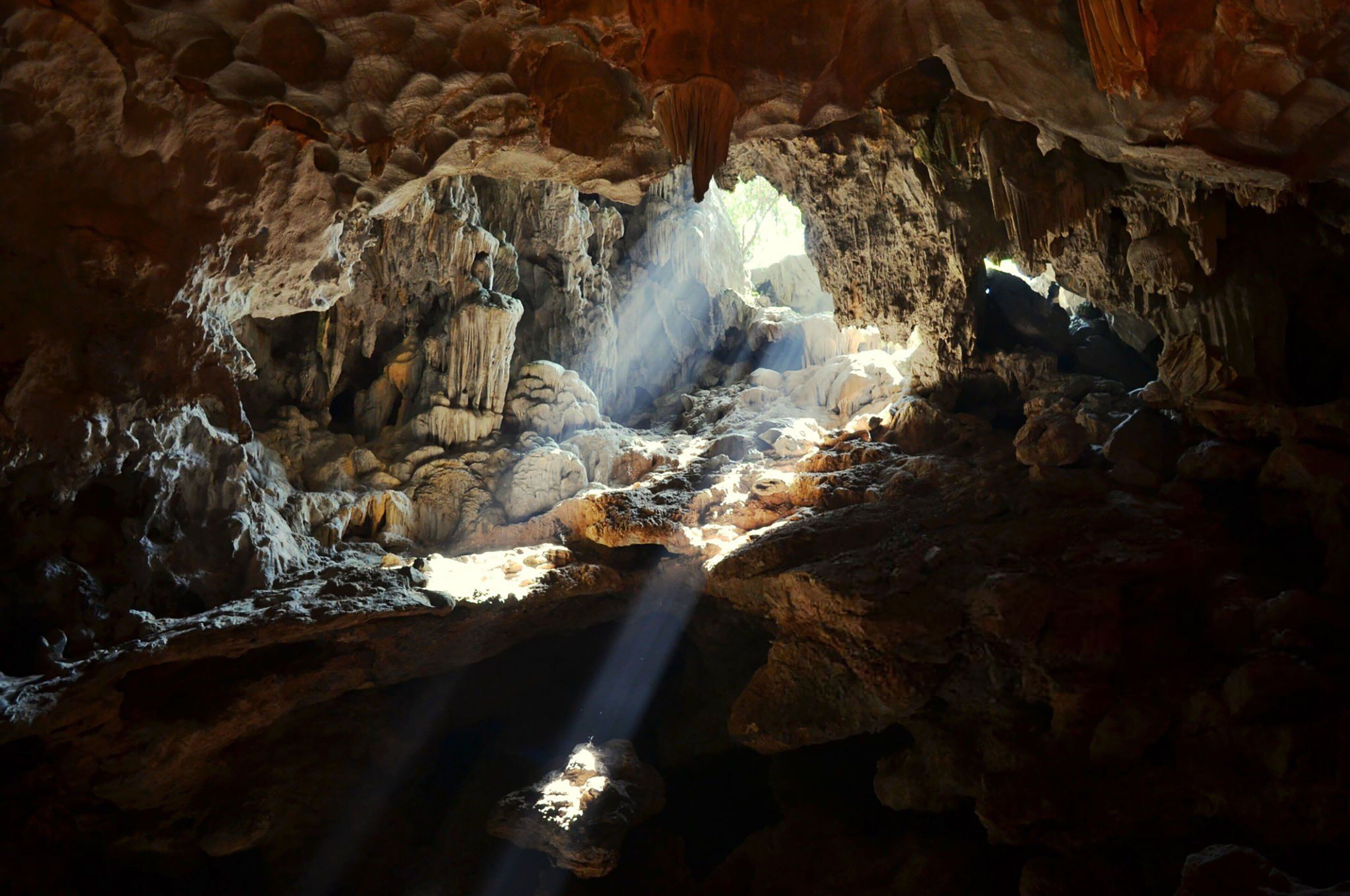 A cave with stalactites and stalagmites, a stream, and natural lighting.