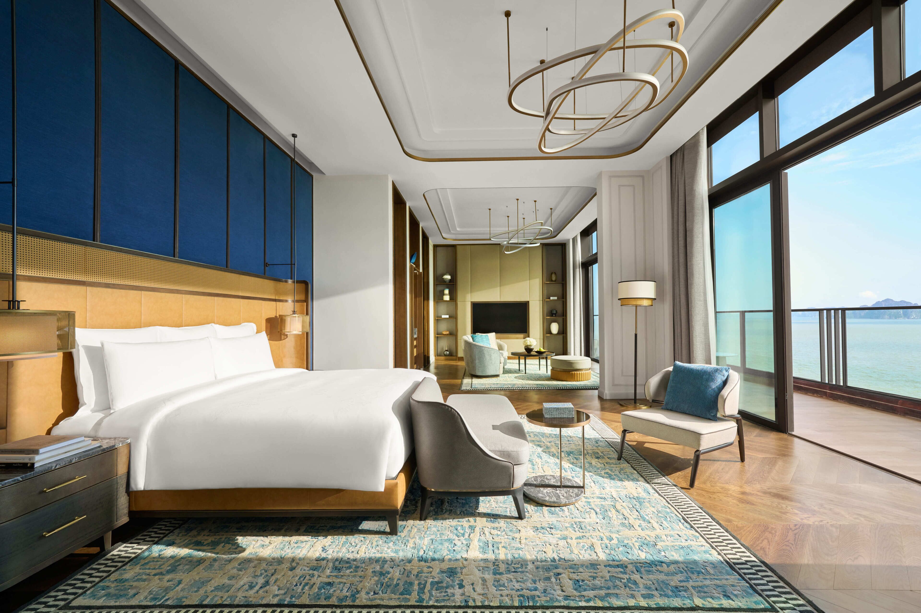 A modern hotel room with a large bed, a seating area with a coffee table, and a view of the sea.