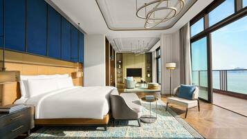 A modern hotel room with a large bed, a seating area with a coffee table, and a view of the sea.