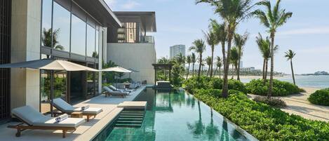 Un resort moderno con piscina, sillones de sol y palmeras.