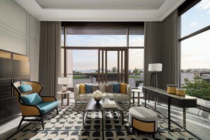Quarto de hotel moderno com uma janela grande, um sofá, uma poltrona, uma mesa de centro e uma pequena mesa com abajur.