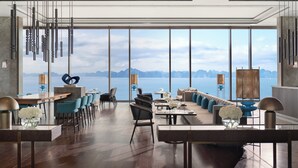 Un espace de restauration moderne avec vue sur la mer, comprenant une longue table, des chaises et un coin bar.