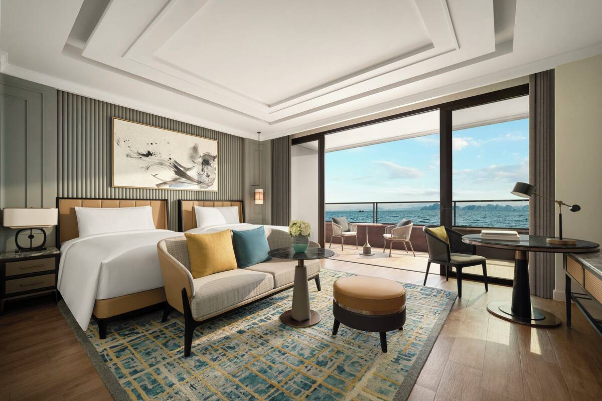 Una habitación de hotel moderna con una cama grande, un sofá, una mesita y un balcón con vista al mar.