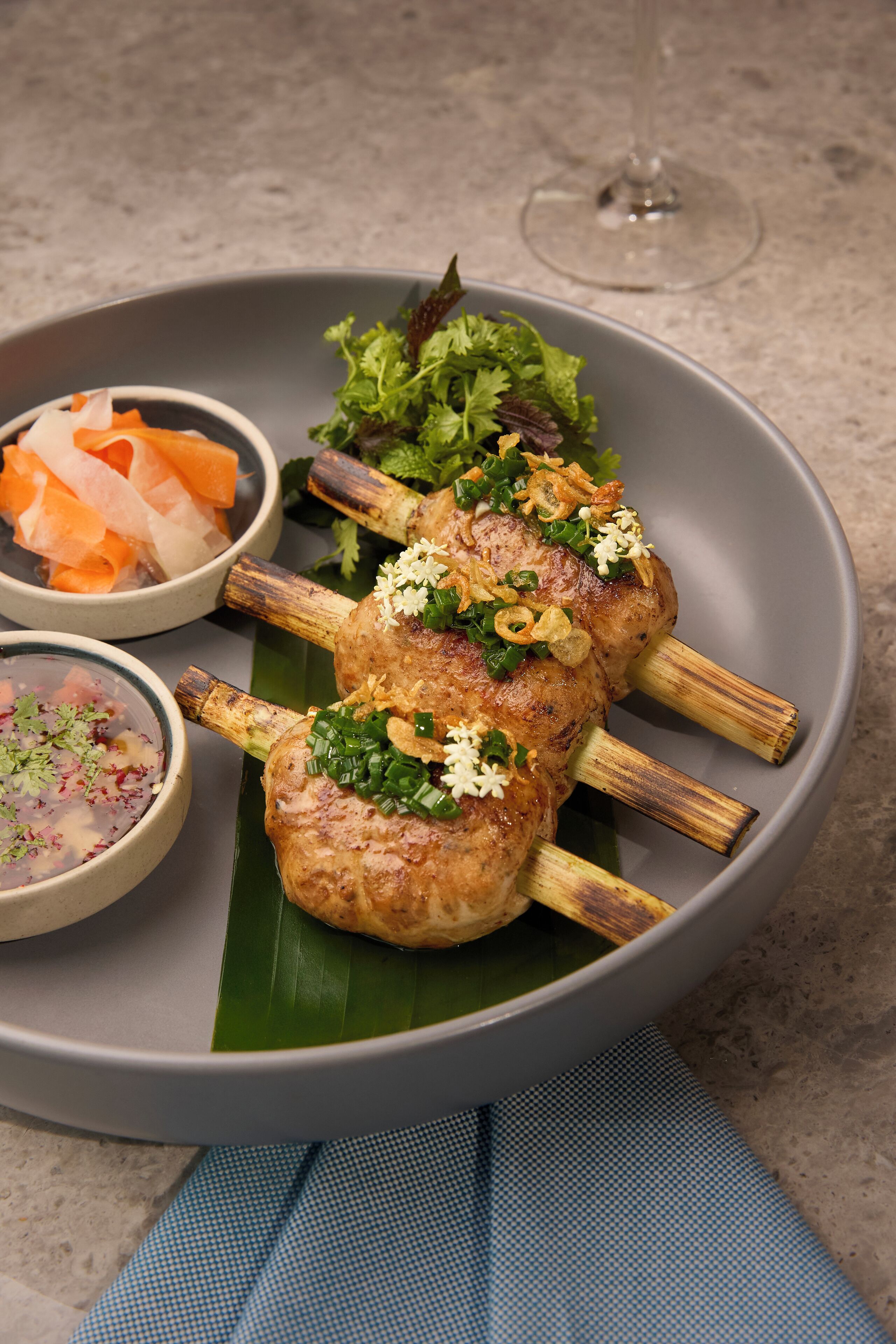 A plate with grilled meat skewers, a bowl of soup, and a glass of wine on a table.
