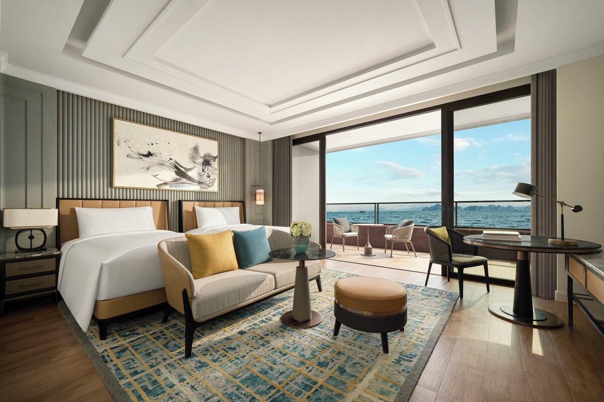 Une chambre d’hôtel moderne dotée d’un grand lit, d’un canapé, d’une petite table et d’un balcon offrant une vue sur la mer.