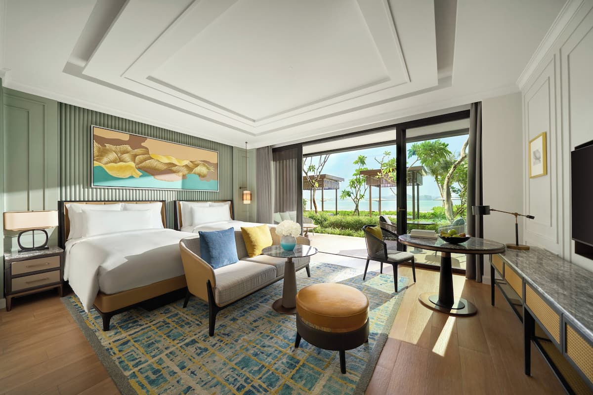 Habitación de hotel con cama, sofá, sillón, mesa de centro y vista al océano.