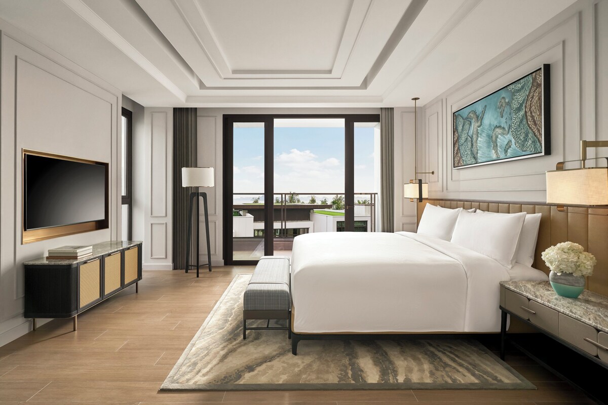 Une chambre d’hôtel moderne dotée d’un grand lit, d’une télévision à écran plat, d’un bureau et d’un balcon avec vue.