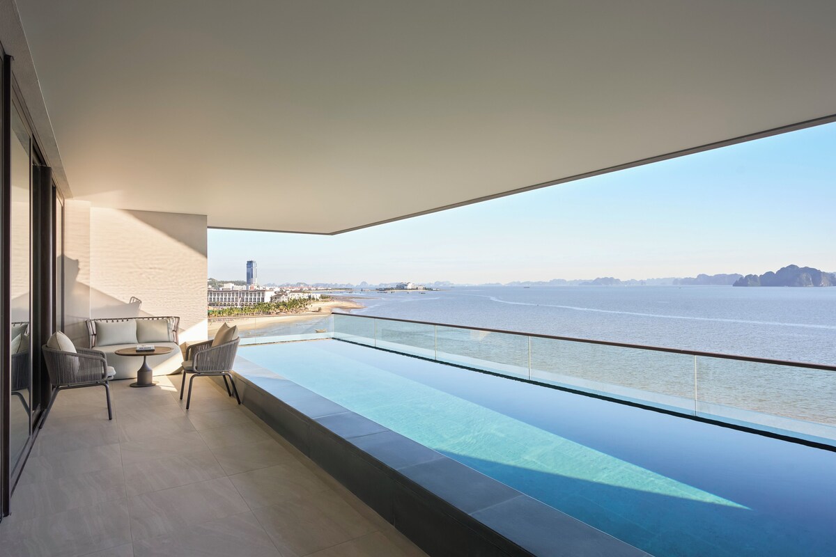 A balcony with a glass barrier overlooking a beach and ocean.