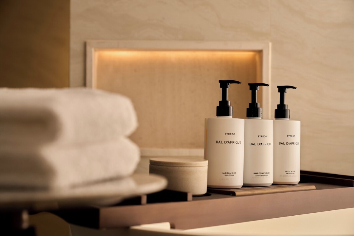 Un meuble-lavabo de salle de bain avec trois flacons de produits capillaires de la marque BYREDO, gamme BAL D'AFRIQUE, et une serviette pliée.