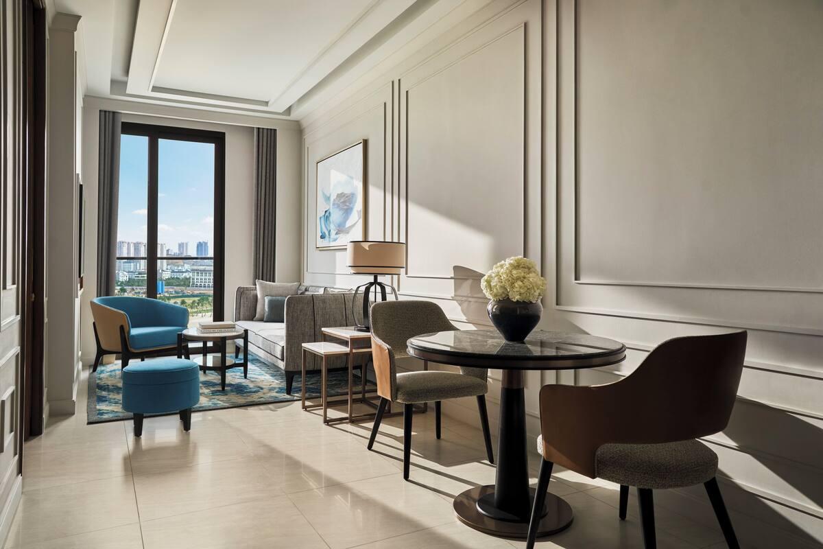 Una habitación de hotel moderna con un ventanal grande, una mesa redonda para comer y un sofá.