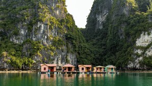 Une rangée de maisons flottantes offrant une vue dégagée sur les falaises et l’eau environnantes.