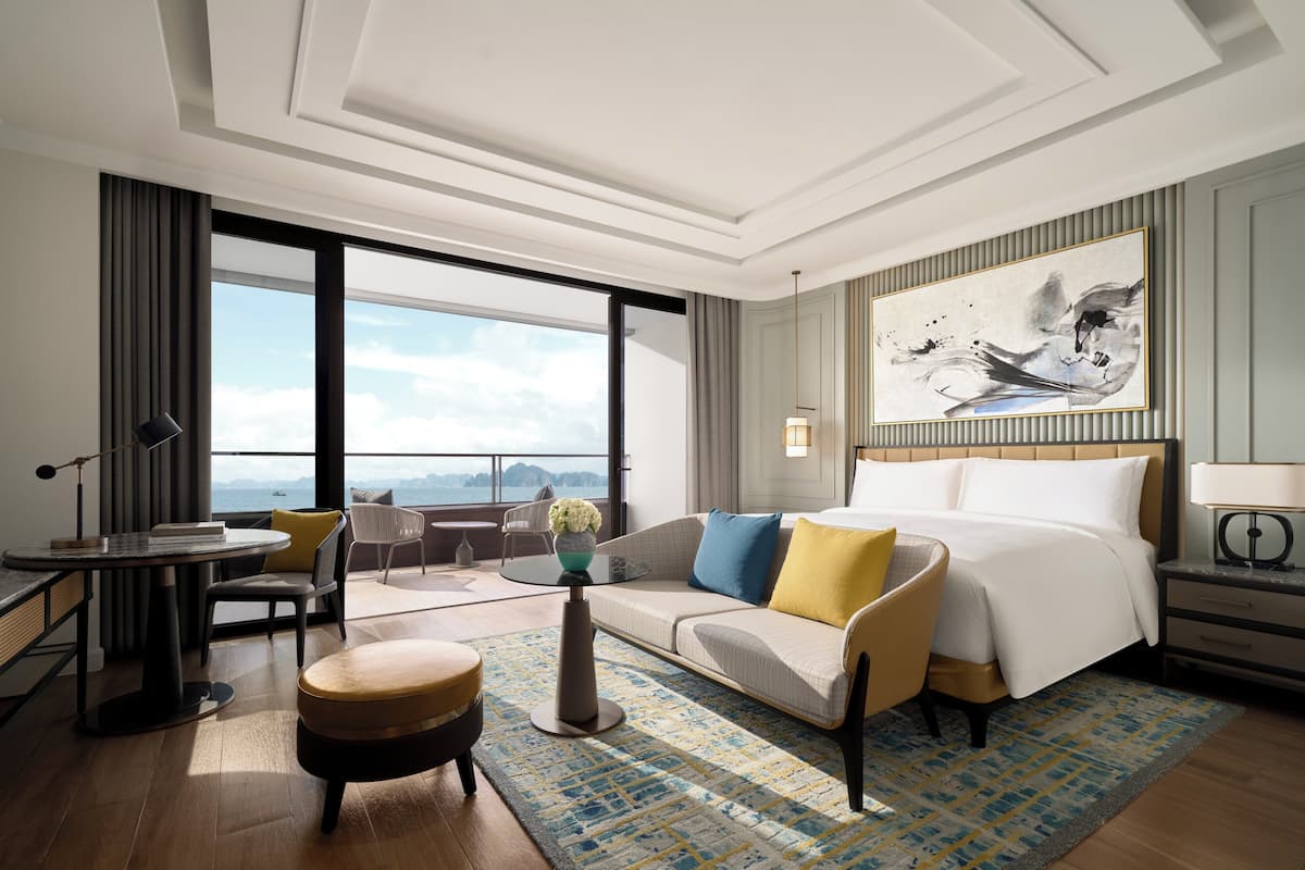 Una habitación de hotel moderna con un ventanal grande, una cama, un sofá, una mesa de centro y un escritorio.