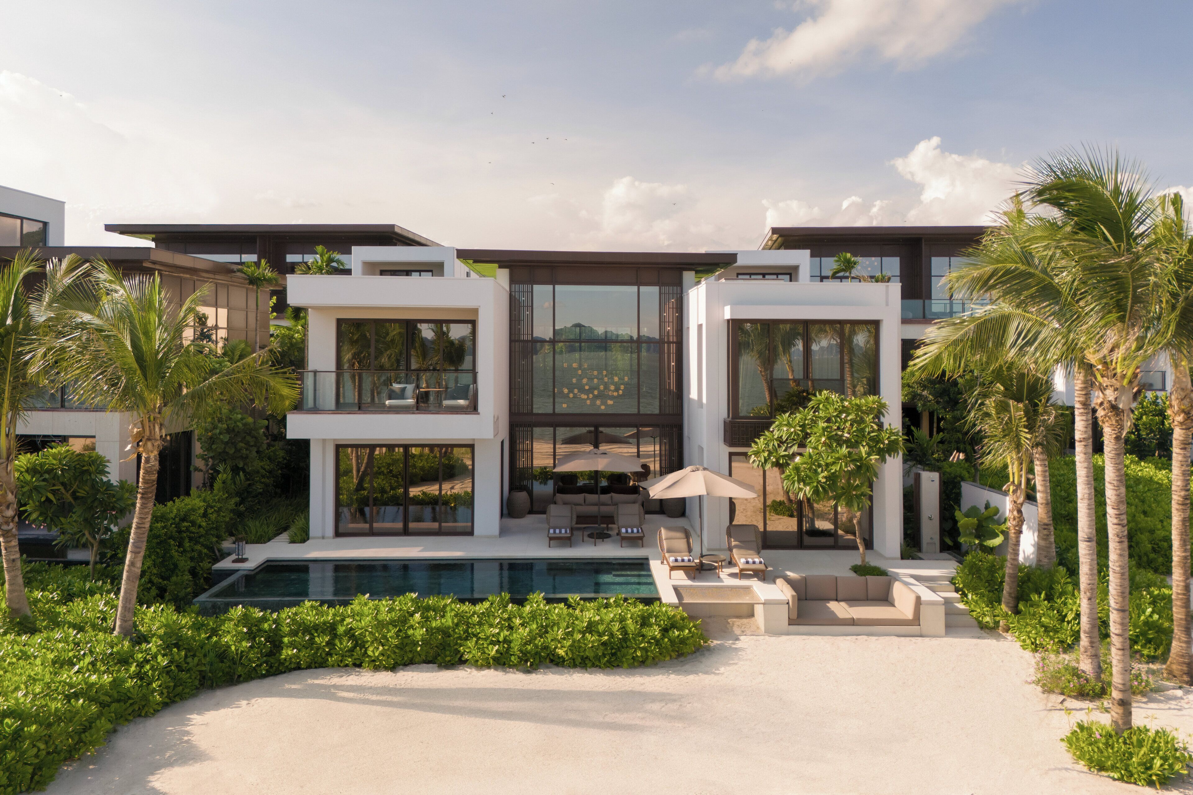 A modern multi-story house with a swimming pool, outdoor seating, and lush greenery.