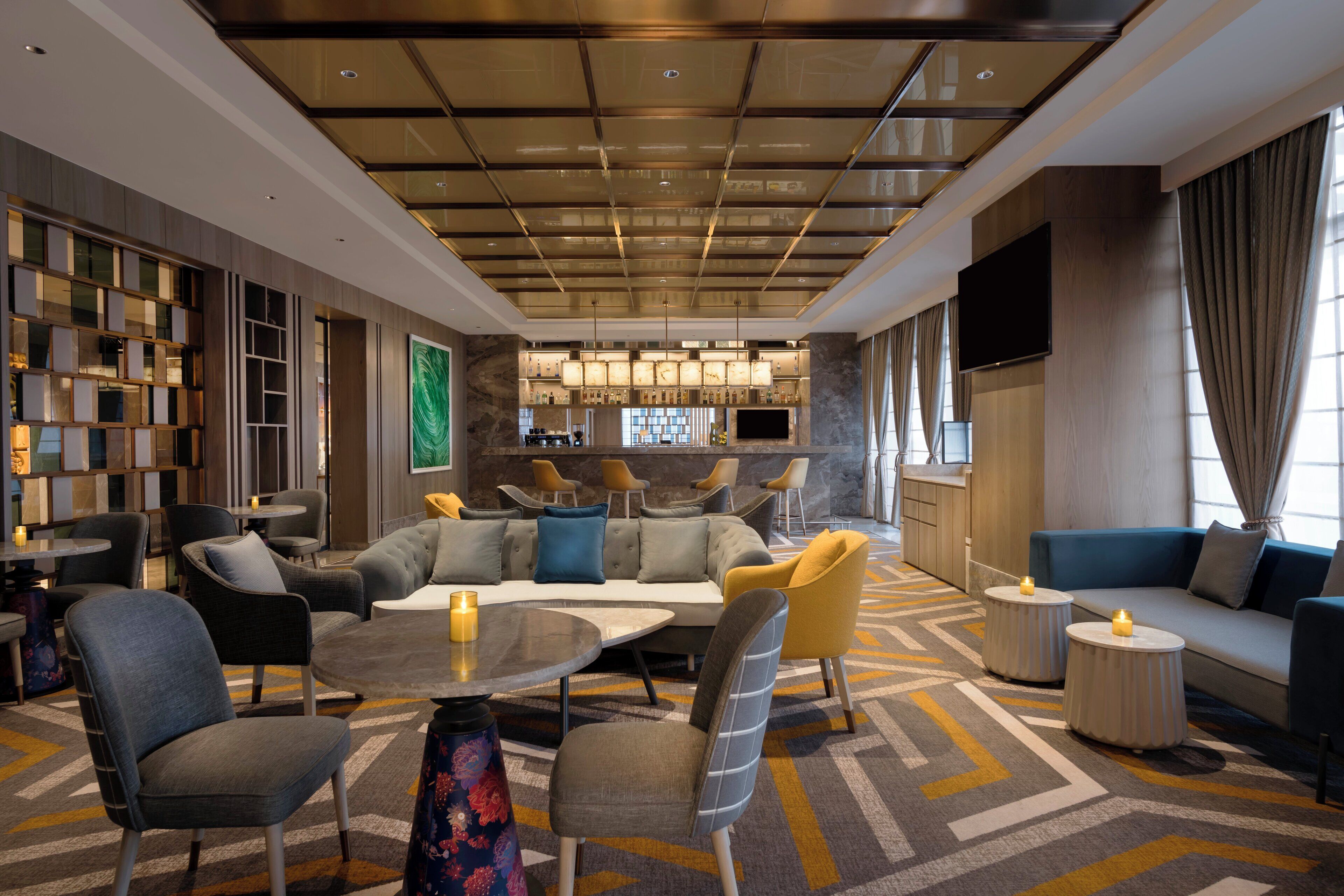 Un moderno vestíbulo de hotel con una zona de estar central, un bar y una televisión.