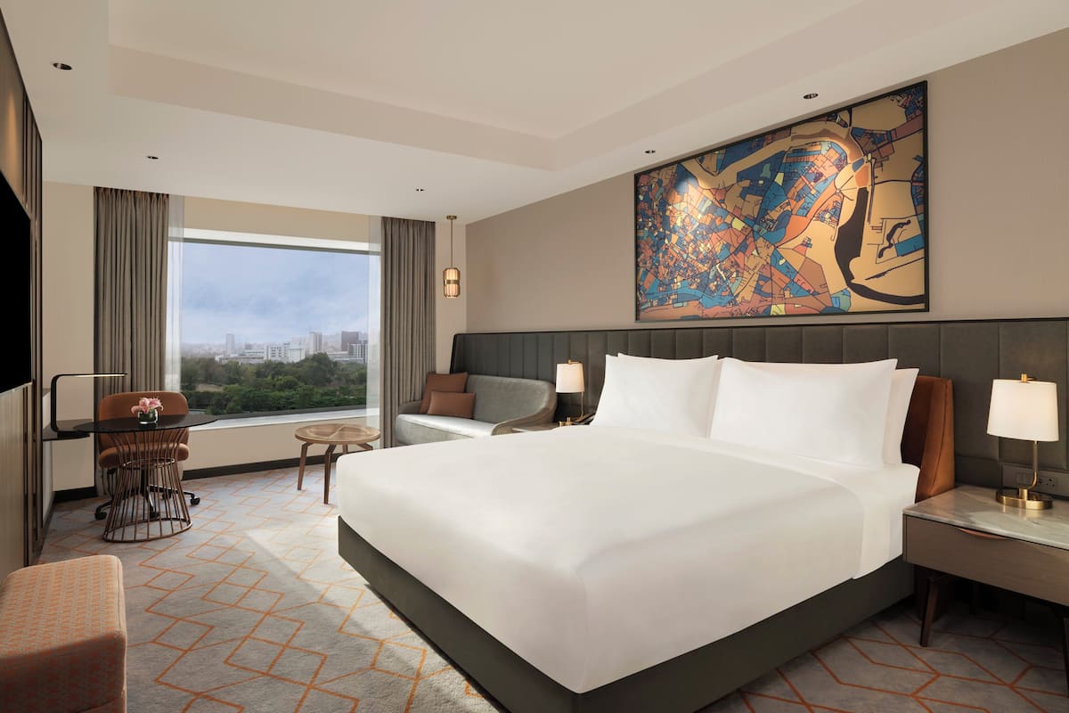 Una habitación de hotel moderna con una cama grande, un escritorio, una silla y vistas de la ciudad a través de un ventanal amplio.