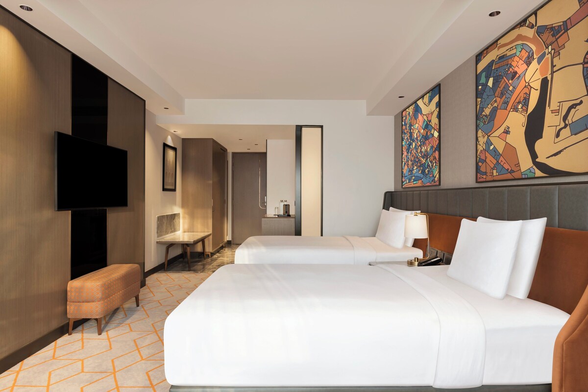 Habitación de hotel con dos camas, un televisor, un escritorio y un cuadro grande en la pared.