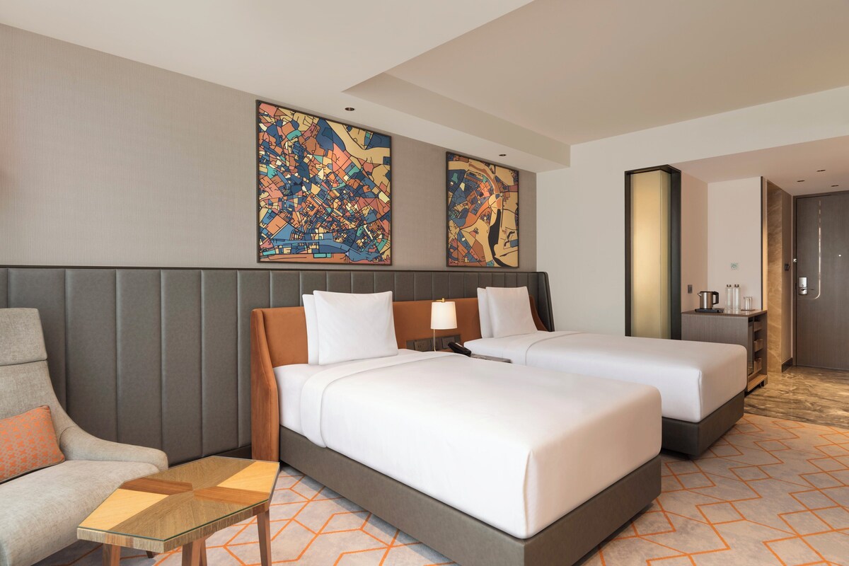 Habitación de hotel con dos camas, un sofá, una mesita y obras de arte en las paredes.