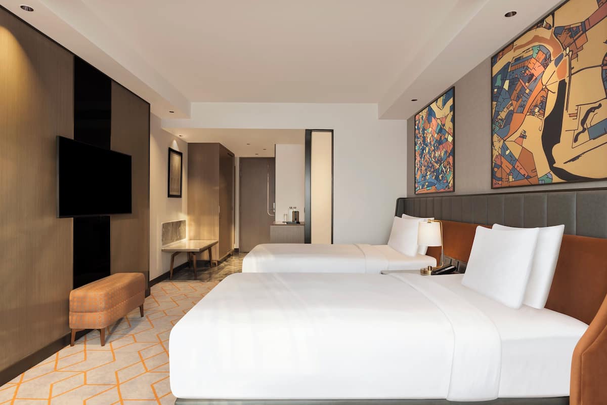 Habitación de hotel con dos camas, un televisor, un escritorio y un cuadro grande en la pared.