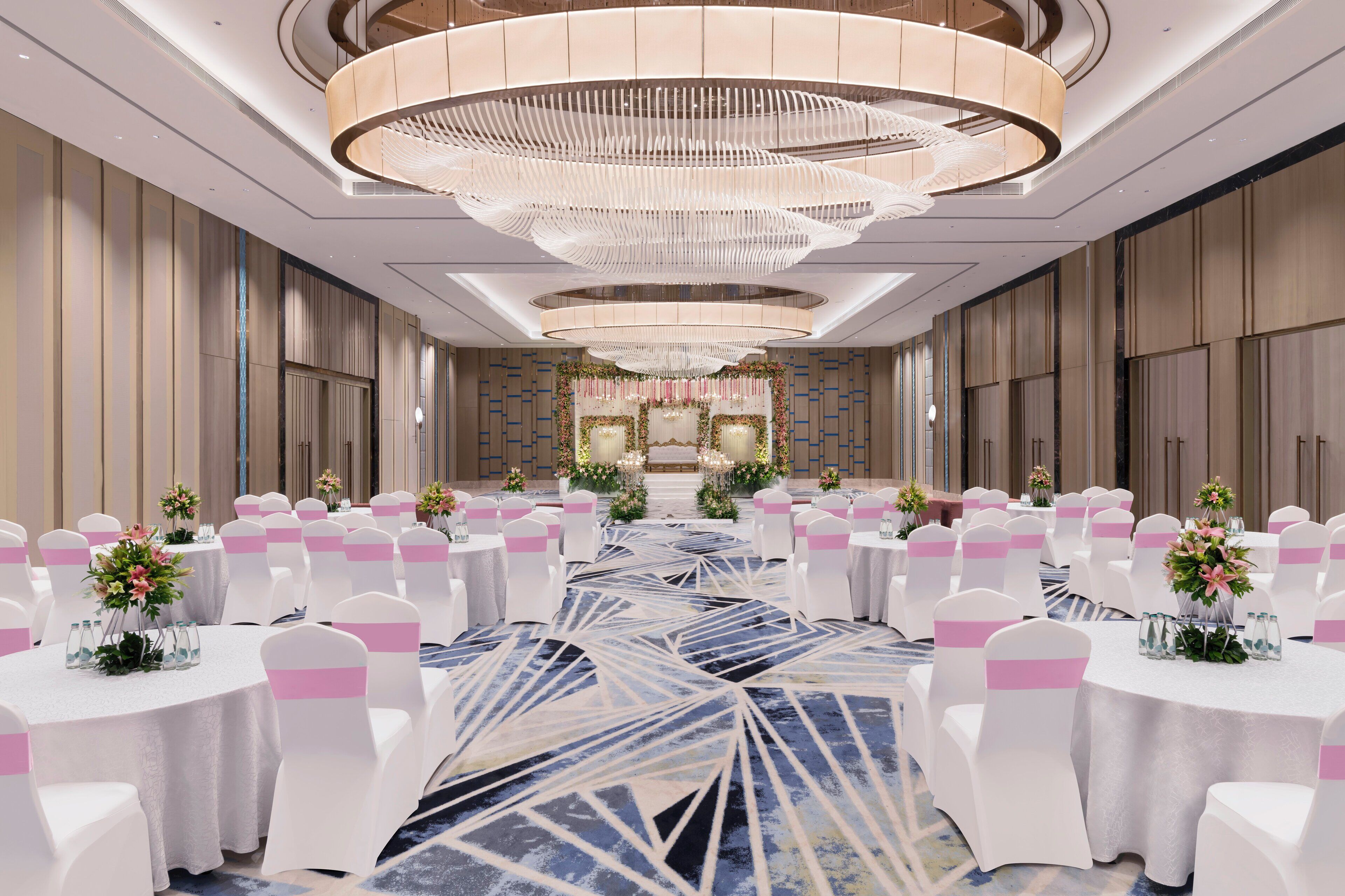 A spacious banquet hall with round tables, white chairs, and a central aisle leading to a stage.