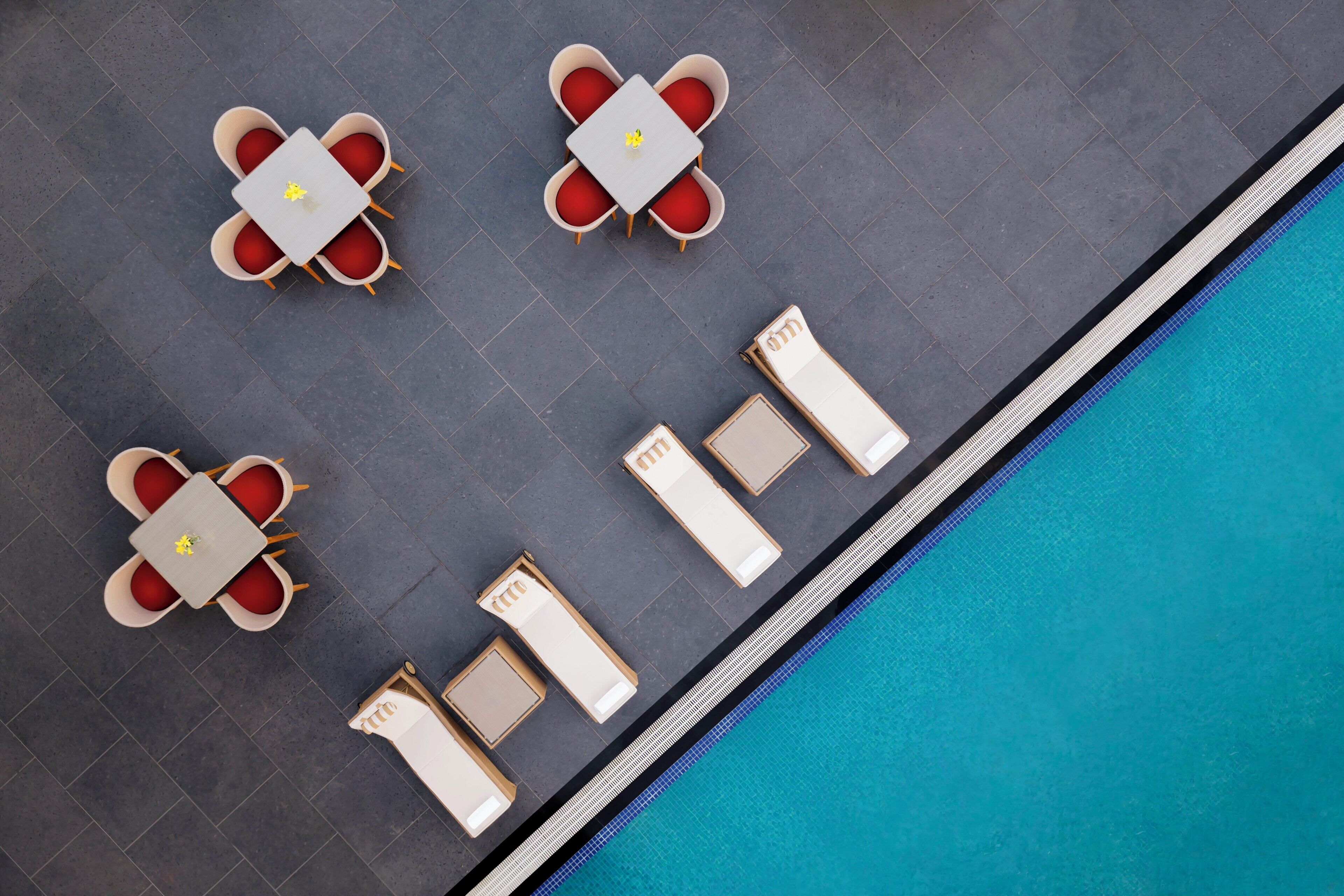 A poolside area with four tables and six lounge chairs arranged around a pool.