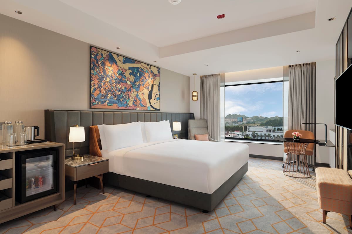 Una habitación de hotel moderna con una cama grande, un escritorio con lámpara, televisión y vistas a la ciudad.