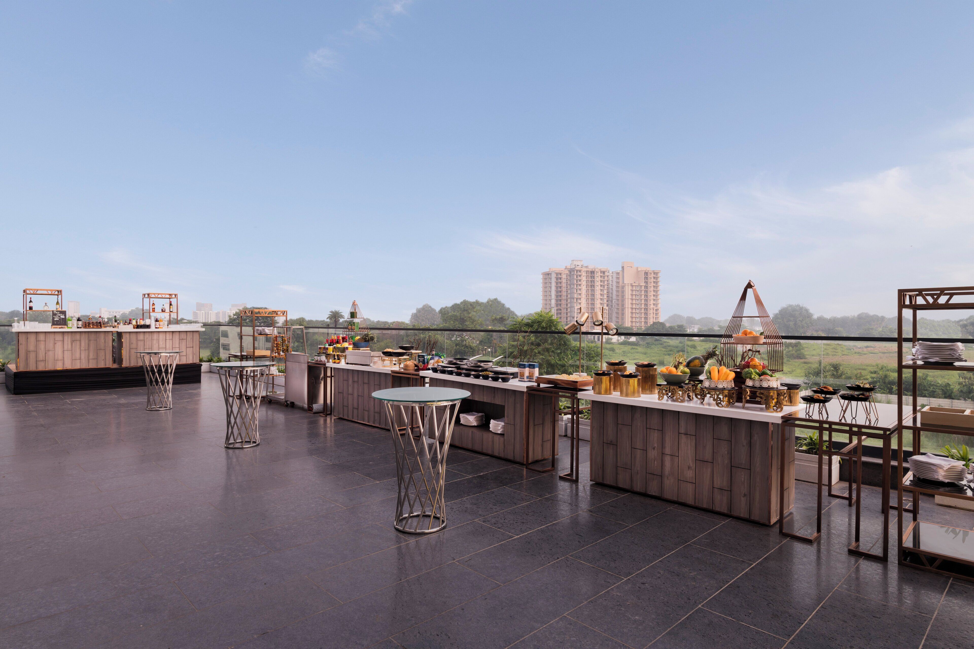 A rooftop bar with a panoramic view, featuring a long counter, several tables, and a variety of bar equipment.