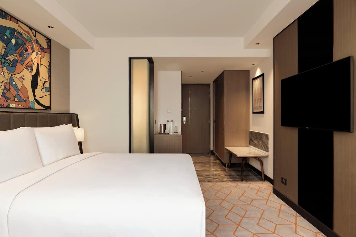 Una habitación de hotel moderna con una cama grande, un televisor de pantalla plana, un escritorio y un baño con ducha e inodoro.