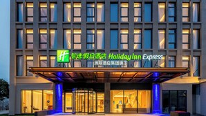 Un hotel Holiday Inn Express con fachada moderna, amplia entrada de vidrio y señalización iluminada.