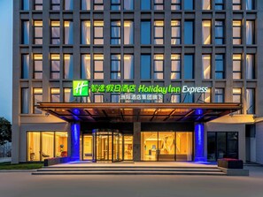 A Holiday Inn Express hotel with a modern facade, large glass entrance, and illuminated signage. - Holiday Inn Express Shanghai PVG Zhuqiao by IHG (Shanghai)