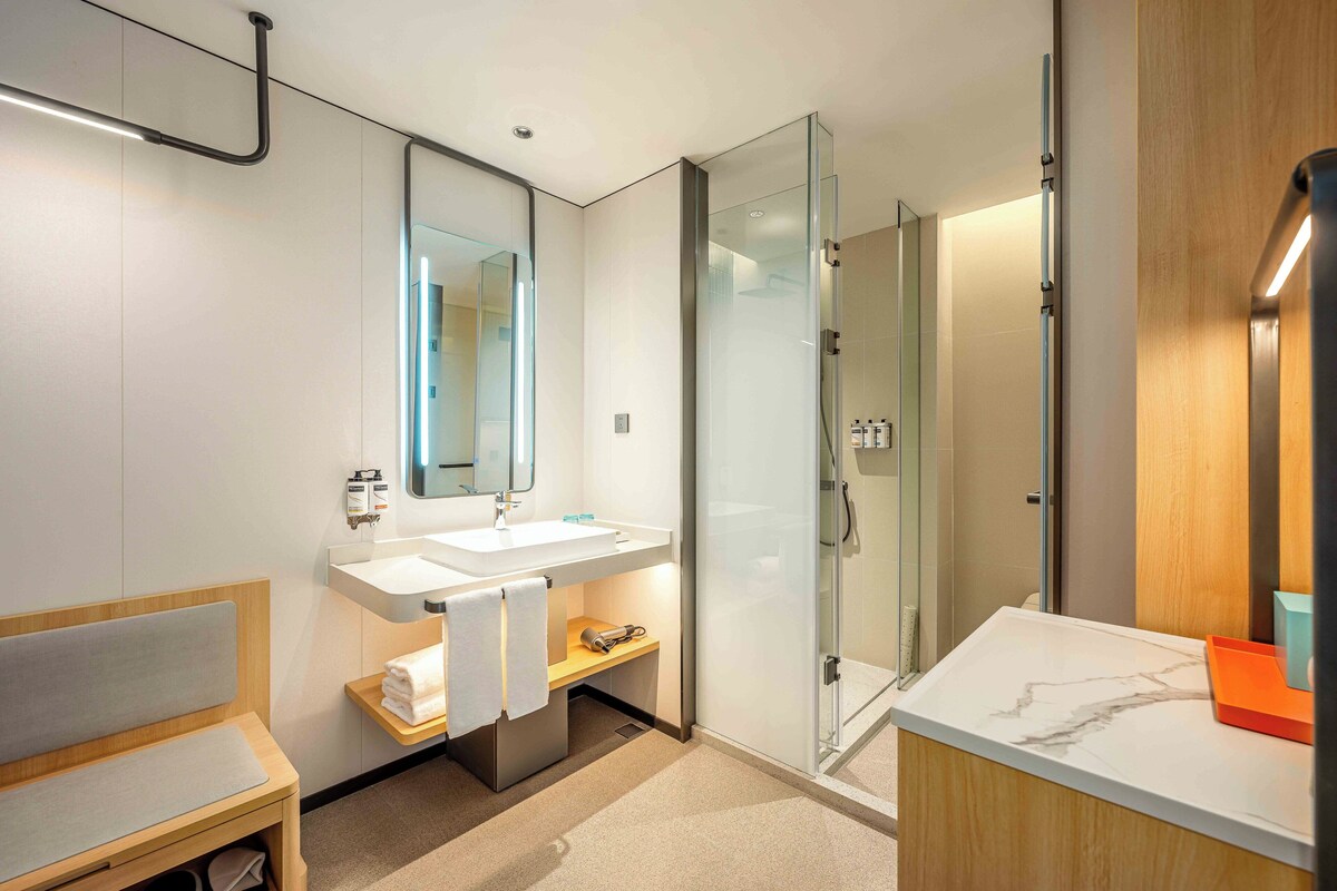 A modern bathroom with a glass shower, a wooden bench, and a marble countertop.