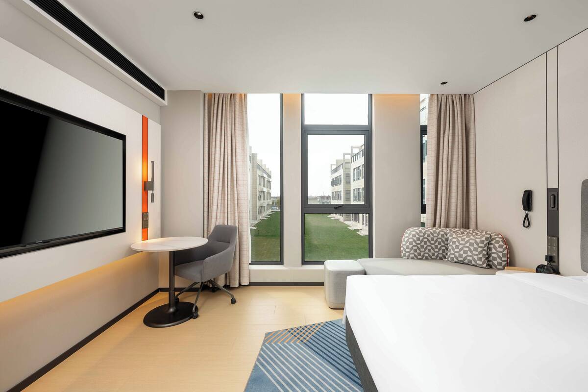 Una habitación de hotel moderna con una cama grande, un escritorio, una silla y un televisor.
