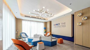 Un área de espera moderna con un sofá modular, sillas anaranjadas y una pared con el texto 'EXPECT THE UNEXPECTED'.