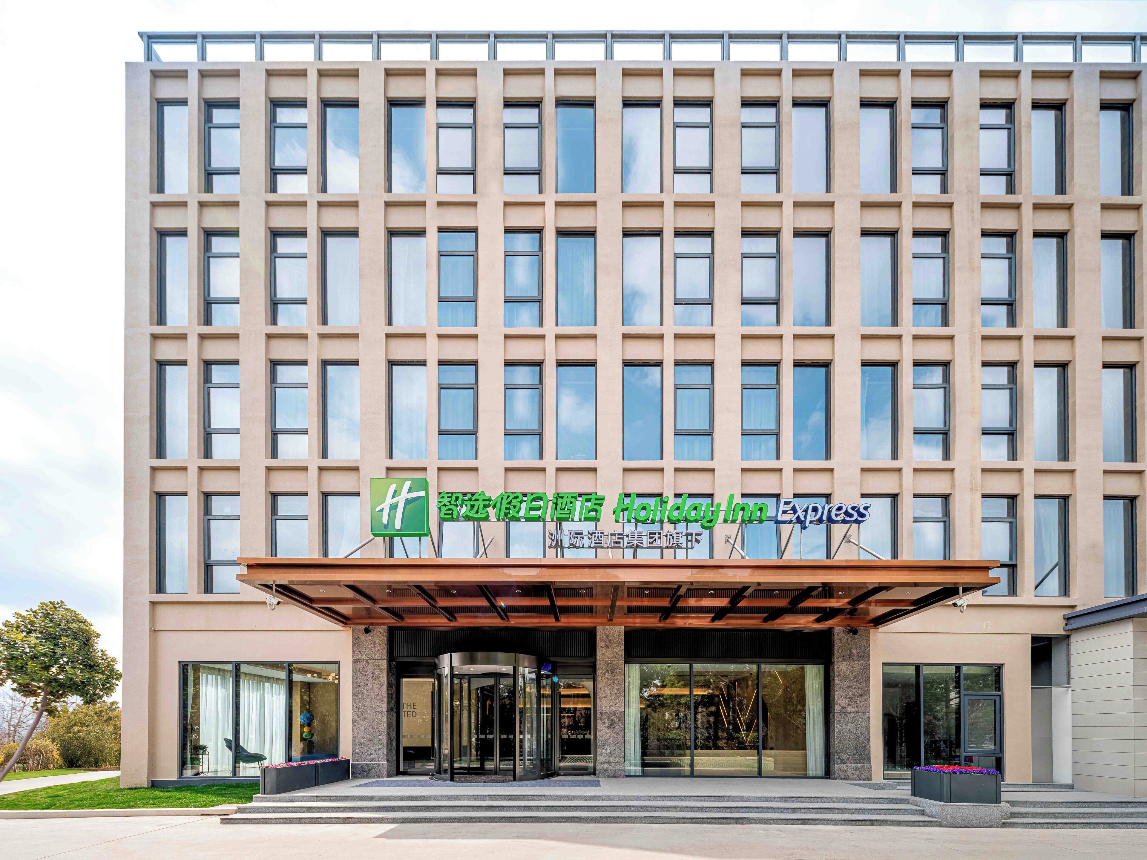 Un moderno edificio de hotel con una entrada grande, un letrero de Holiday Inn Express y un letrero verde con caracteres chinos.