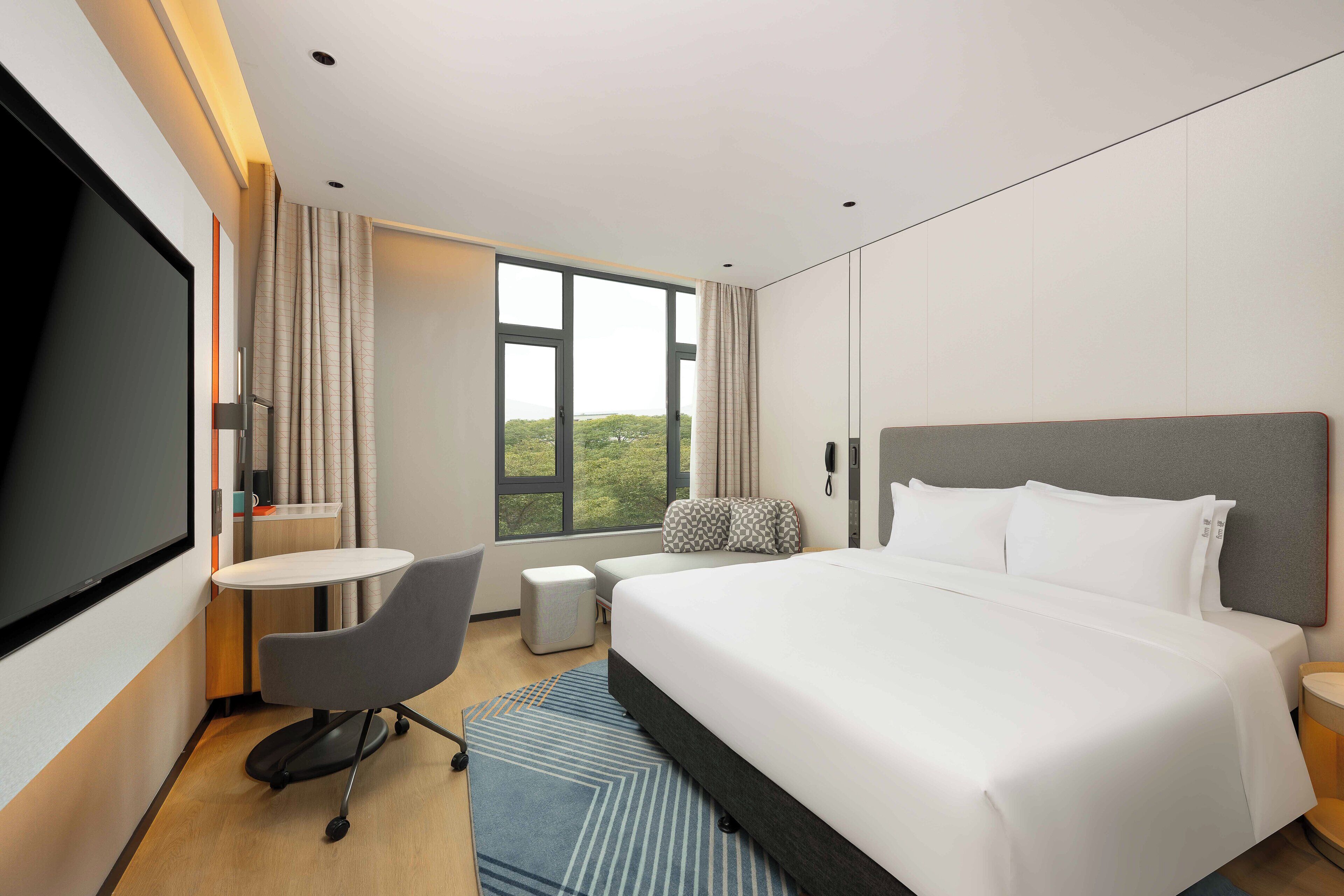 Una habitación de hotel moderna con una cama grande, un escritorio, una silla y un televisor.