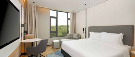 A modern hotel room with a large bed, a desk, a chair, and a TV.