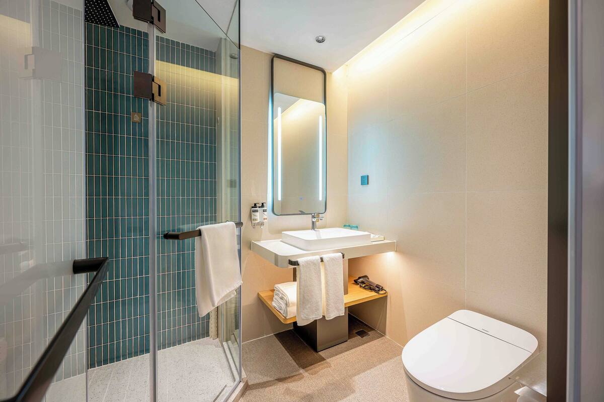 Un baño moderno con cabina de ducha de vidrio, un lavabo blanco y un inodoro.