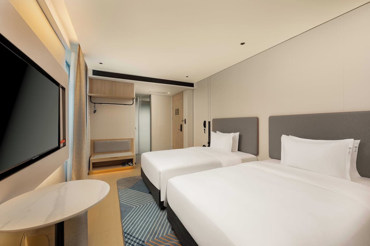 Habitación de hotel con dos camas, televisión, escritorio y zona de ducha.