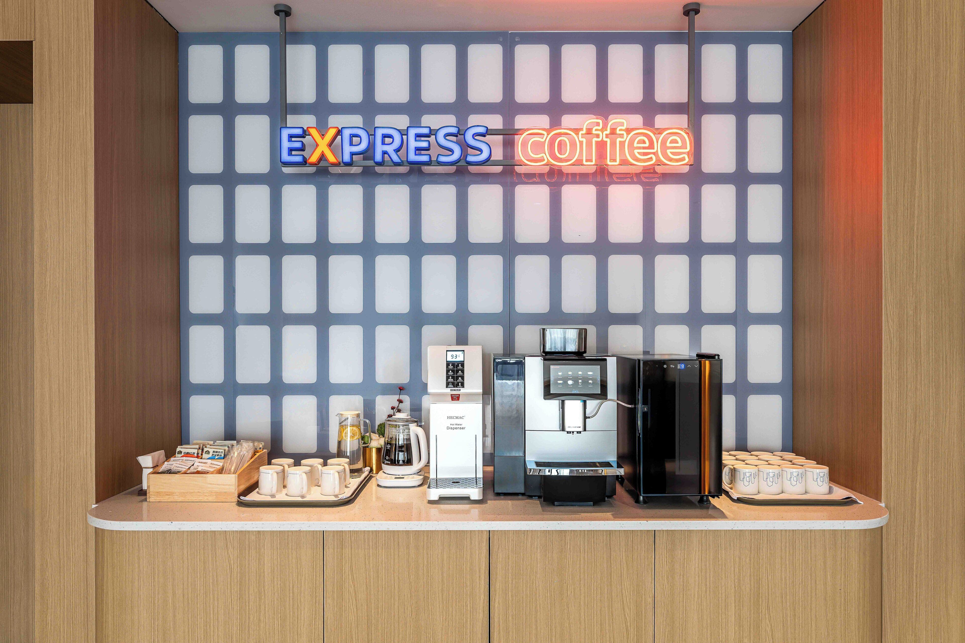 A coffee station with a neon sign reading "EXPRESS coffee," a coffee maker, a refrigerator, and a tray with cups.