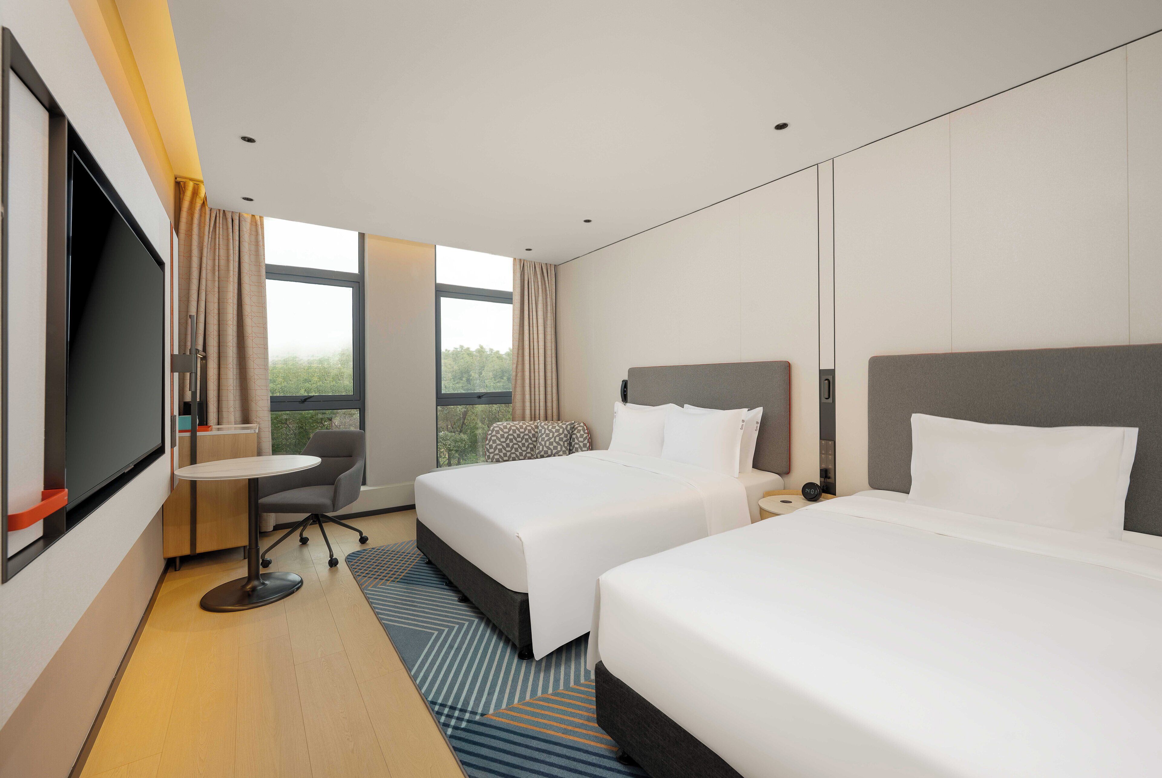 Quarto de hotel com duas camas, uma televisão, uma mesa pequena e vista para o exterior.