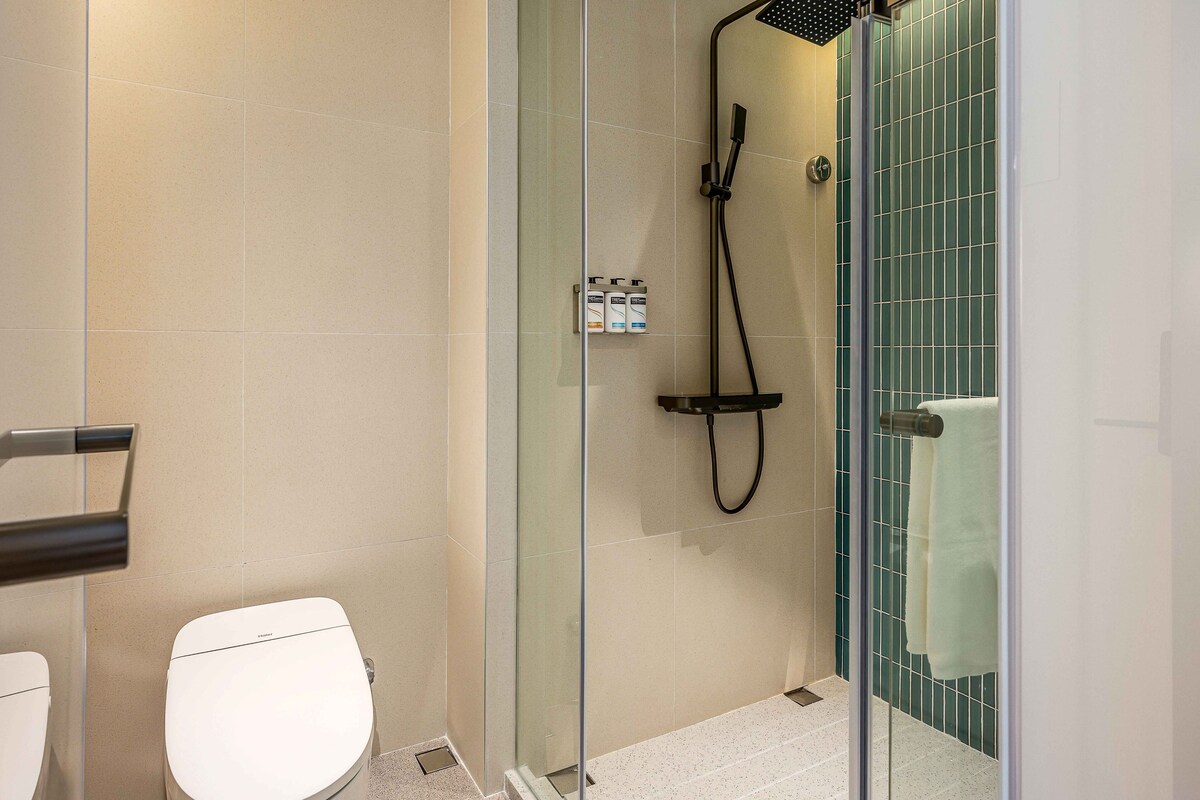 A modern bathroom with a glass-enclosed shower, a toilet, and a towel rack.