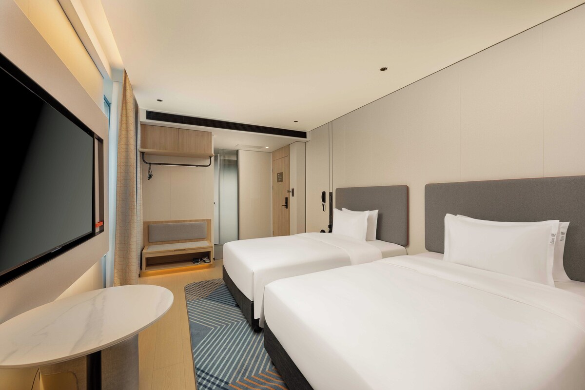 A hotel room with two beds, a TV, a desk, and a shower area.