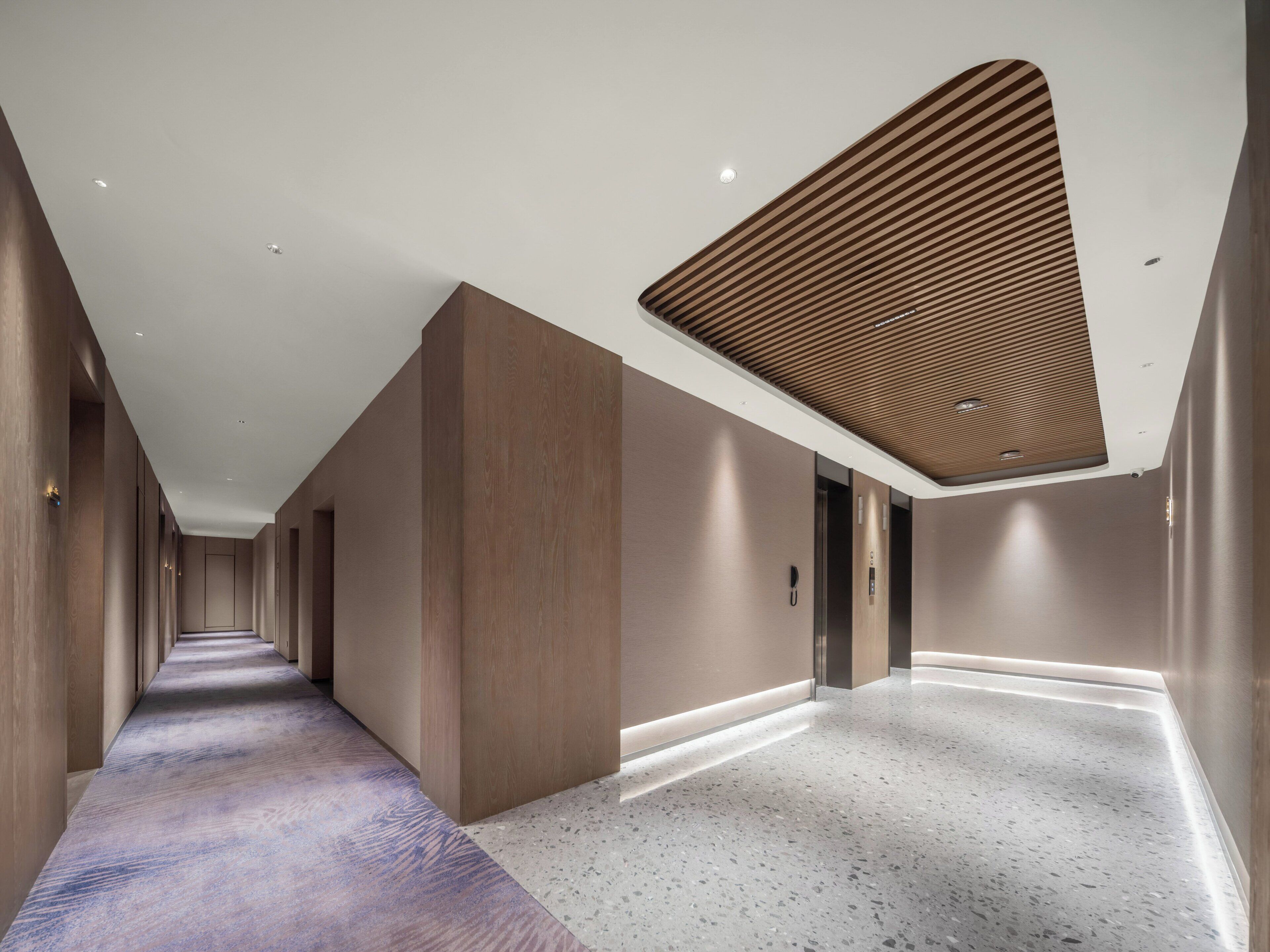 Un couloir d’hôtel moderne, avec un long couloir, des murs lambrissés en bois et un sol à motifs.